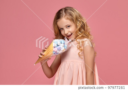 Little girl with a blond curly hair, in a pink dress is posing with an ice-cream Little girl with a blond curly hair, in a pink dress is posing with an ice-cream 97977281