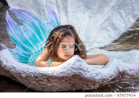 A beautiful girl in a turquoise mermaid costume in a large sea shell 97977454
