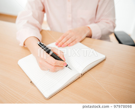 Close up of a woman's hands writing in a notebook placed on a wooden table, home office and work concept, plans and thoughts Close up of a woman's hands writing in a notebook placed on a wooden table, home office and work concept, plans and thoughts 97978098