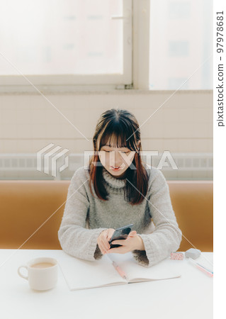 Photo of a young female college student touching a smartphone while studying in a cafe Photo of a young female college student touching a smartphone while studying in a cafe 97978681
