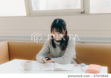 一名年輕女大學生在咖啡館學習時觸摸智能手機的照片 97978688