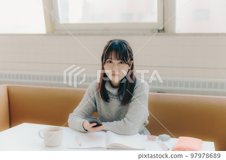 一名年輕女大學生在咖啡館學習時觸摸智能手機的照片 一名年輕女大學生在咖啡館學習時觸摸智能手機的照片 97978689