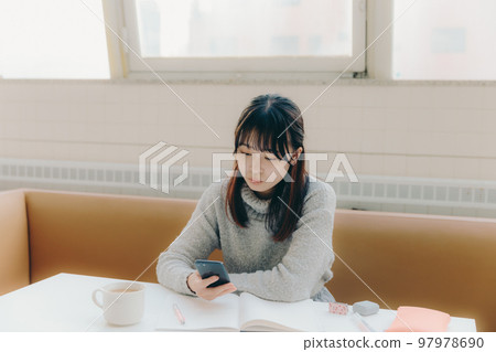 一名年輕女大學生在咖啡館學習時觸摸智能手機的照片 97978690