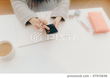 一名年輕女大學生在咖啡館學習時觸摸智能手機的照片 一名年輕女大學生在咖啡館學習時觸摸智能手機的照片 97978696