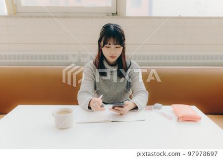 一名年輕女大學生在咖啡館學習時觸摸智能手機的照片 一名年輕女大學生在咖啡館學習時觸摸智能手機的照片 97978697