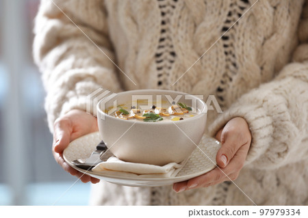 Young woman with bowl of cream soup on blurred background, closeup 97979334