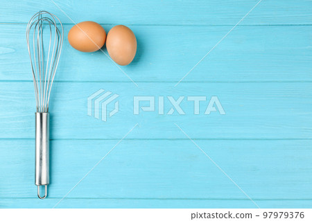 Raw eggs and whisk on light blue wooden table, top view with space for text. Baking pie 97979376