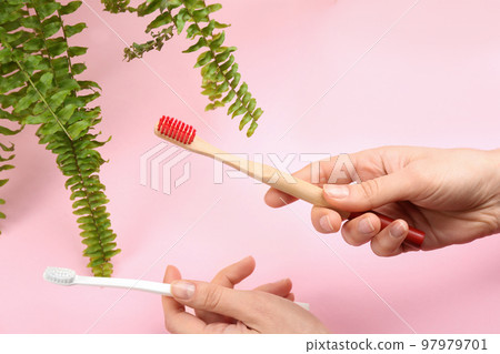 Woman holding natural bamboo and plastic toothbrushes on pink background Woman holding natural bamboo and plastic toothbrushes on pink background 97979701