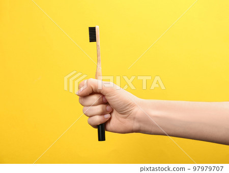 Woman holding bamboo toothbrush on yellow background, closeup Woman holding bamboo toothbrush on yellow background, closeup 97979707