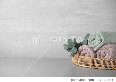 Wicker tray with rolled bath towels and eucalyptus branch on grey table. Space for text 97979783