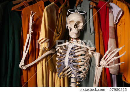 Artificial human skeleton model among clothes in wardrobe 97980215