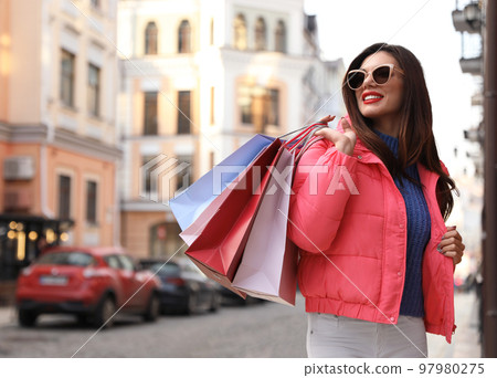 Beautiful young woman with shopping bags on city street 97980275