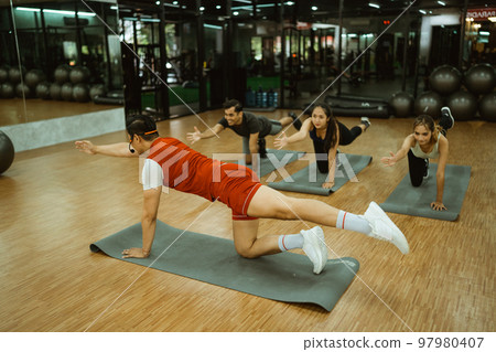 Male instructor demonstrating balance and muscle strength movements with mats 97980407