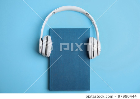 Book and modern headphones on light blue background, top view 97980444