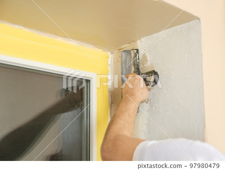 Man plastering window area with putty knife indoors, closeup. Interior repair 97980479