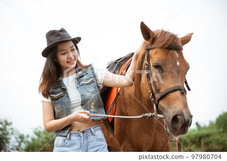 beautiful asian cowboy girl standing beside horse on outdoor background beautiful asian cowboy girl standing beside horse on outdoor background 97980704