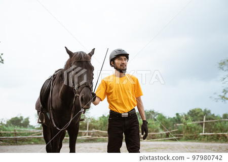 Male equestrian in equipment standing next to horse Male equestrian in equipment standing next to horse 97980742