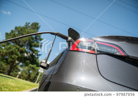 Black electric car charging outdoors in summer. Black electric car charging outdoors in summer. 97987856