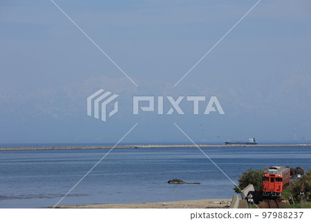 JR Himi Line Kiha 40 running along the Amaharashi coast against the background of the Tateyama mountain range in spring Etchoku-Amaharashi 97988237