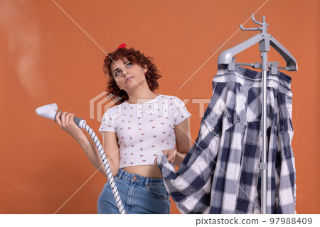 A girl with curly hair, quite distracted while ironing with a steamer. 97988409