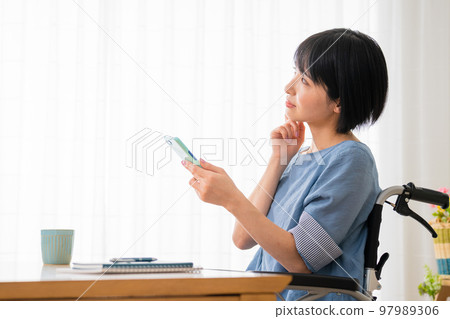 坐在輪椅上操作智能手機的年輕女性 多元社會的形象 坐在輪椅上操作智能手機的年輕女性 多元社會的形象 97989306