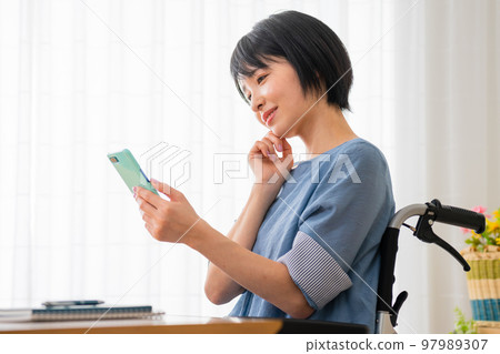 坐在輪椅上操作智能手機的年輕女性 多元社會的形象 坐在輪椅上操作智能手機的年輕女性 多元社會的形象 97989307