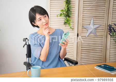 A young woman operating a smartphone while sitting in a wheelchair Image of a diverse society A young woman operating a smartphone while sitting in a wheelchair Image of a diverse society 97989308
