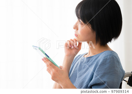 坐在輪椅上操作智能手機的年輕女性 多元社會的形象 坐在輪椅上操作智能手機的年輕女性 多元社會的形象 97989314