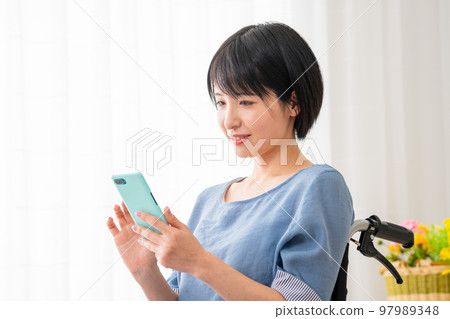 坐在輪椅上操作智能手機的年輕女性 多元社會的形象 坐在輪椅上操作智能手機的年輕女性 多元社會的形象 97989348