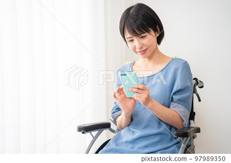 A young woman operating a smartphone while sitting in a wheelchair Image of a diverse society A young woman operating a smartphone while sitting in a wheelchair Image of a diverse society 97989350