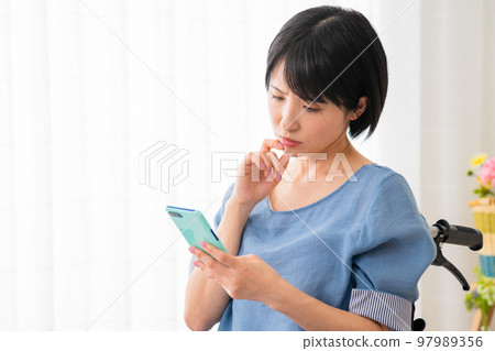 A young woman operating a smartphone while sitting in a wheelchair Image of a diverse society A young woman operating a smartphone while sitting in a wheelchair Image of a diverse society 97989356
