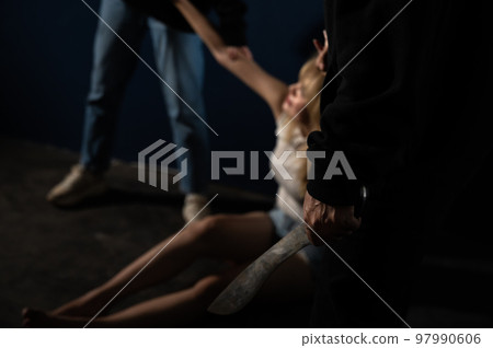 Violent men standing with knife in hand and threatens woman sitting on the floor in abandoned room. Violent men standing with knife in hand and threatens woman sitting on the floor in abandoned room. 97990606