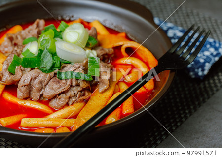 黑盤上放著辣味韓國菜 Tteokbokki，配有牛肉、蔬菜和魚餅 97991571