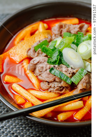 Spicy Korean food Tteokbokki with beef, vegetables and fish cake served on a black plate 97991587