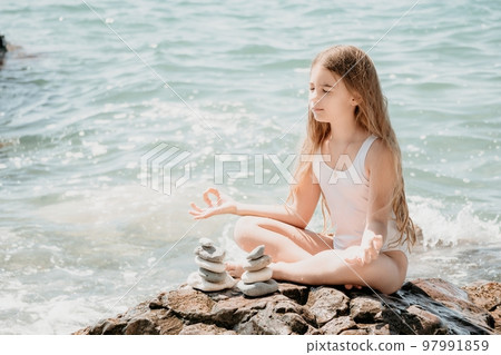 Woman with daughter bilds stones pyramid on seashore on a sunny day on the blue sea background. Happy family holidays. Pebble beach, calm sea. Concept of happy vacation on the sea, meditation, spa Woman with daughter bilds stones pyramid on seashore on a sunny day on the blue sea background. Happy family holidays. Pebble beach, calm sea. Concept of happy vacation on the sea, meditation, spa 97991859