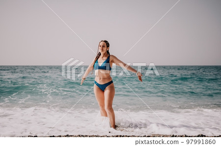 A tourist woman in blue bikini on beach enjoys the turquoise sea during her summer holiday. Rear view. Beach vacation. woman with braids dreadlocks standing with her arms raised enjoying beach ocean. A tourist woman in blue bikini on beach enjoys the turquoise sea during her summer holiday. Rear view. Beach vacation. woman with braids dreadlocks standing with her arms raised enjoying beach ocean. 97991860