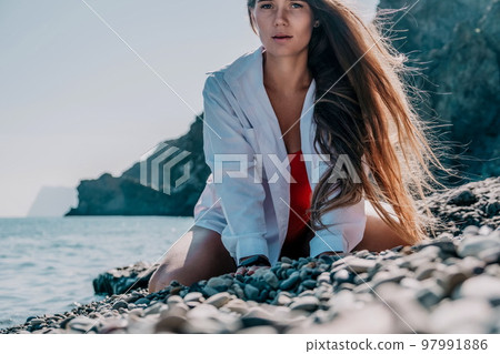 Young woman in red bikini on Beach. Girl lying on pebble beach and enjoying sun. Happy lady with long hair in bathing suit chilling and sunbathing by turquoise sea ocean on hot summer day. Close up 97991886