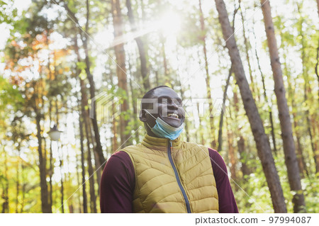 Handsome african american man wearing casual clothes take off medical mask smiling happy walking in city park - end of pandemic 97994087