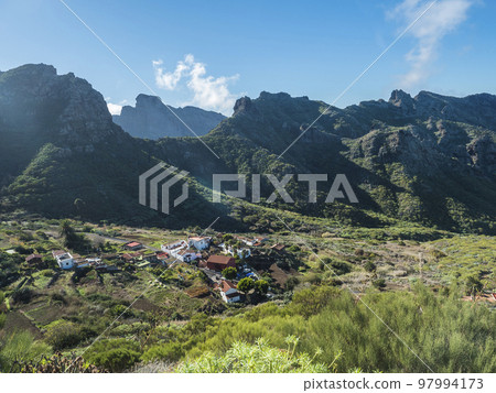 Dramatic lush green picturesque valley with old village Los Carrizales . Landscape with sharp rock formation, hills and cliffs seen from mountain road, Tenerife, Canary Islands, Spain. sunny winter 97994173