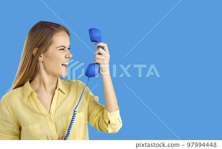 Angry irritated young woman standing talking on telephone screaming swearing isolated on blue turquoise colour background studio Angry irritated young woman standing talking on telephone screaming swearing isolated on blue turquoise colour background studio 97994448