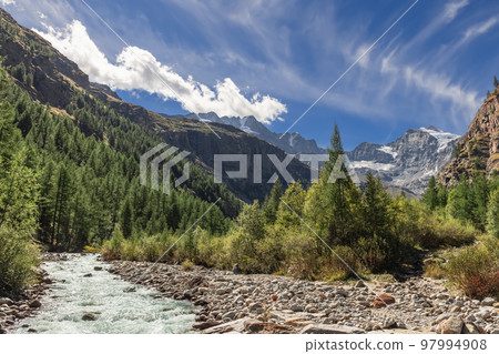 Foaming water stream rushes along channel lined with pebbles in Gran Paradiso National Park 97994908