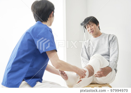 Doctor bandaging middle-aged man's leg Doctor bandaging middle-aged man's leg 97994970