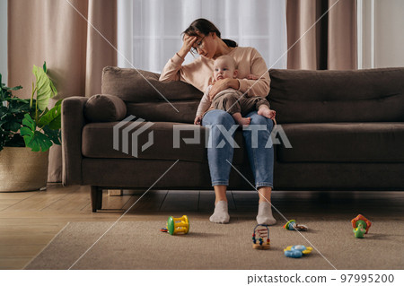 Young tired mother with headache suffering from postnatal depression 97995200