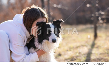 Caucasian woman hugging her dog Border Collie while sitting on a bench in autumn park. 97996843