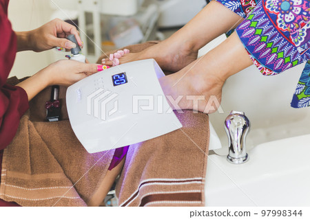 womans foot with a pedicure under UV lamp for drying varnish. womans foot with a pedicure under UV lamp for drying varnish. 97998344