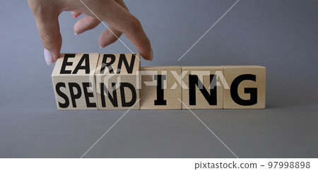 Earning and Spending symbol. Businessman hand. Turned cubes with words Earning and Spending. Beautiful grey background. Business and Earning and Spending concept. Copy space Earning and Spending symbol. Businessman hand. Turned cubes with words Earning and Spending. Beautiful grey background. Business and Earning and Spending concept. Copy space 97998898