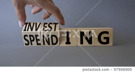 Investing and Spending symbol. Businessman hand. Turned cubes with words Investing and Spending. Beautiful grey background. Business and Investing and Spending concept. Copy space Investing and Spending symbol. Businessman hand. Turned cubes with words Investing and Spending. Beautiful grey background. Business and Investing and Spending concept. Copy space 97998900