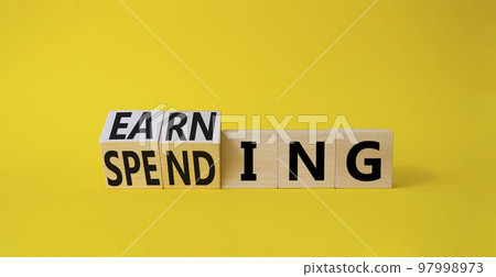 Earning and Spending symbol. Turned cubes with words Earning and Spending. Beautiful yellow background. Business and Earning and Spending concept. Copy space 97998973