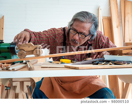 Happy Asian senior man is enjoying his hobby by diligently painting birdhouses in the workshop. 98000510