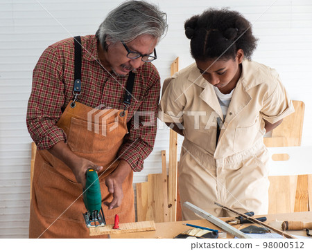 Teenaged girls learn to use an electronic saw and play with their grandfather in the wooden workshop, a concept for enhancing the development and thinking of children. 98000512